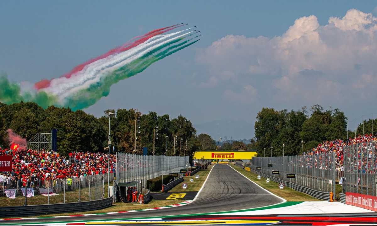 Formula 1 cars at full throttle on Monza's main straight with DRS open and grandstands in the background